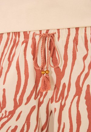 Puuvillased laisad lühikesed püksid beezal põhjal ja roostepunase zebra triibumustriga. Omab paelaga vööd, millel on puidust helmed ja tups.