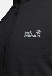 Zwarte fleecejas met gestructureerde stof, kwartrits en reflecterend "Jack Wolfskin"-logo op de linkerborst.