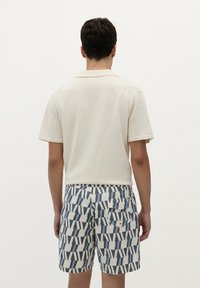 Polo shirt alb cu mâneci scurte, asortat cu pantaloni scurți cu model în albastru și alb, având dungi verticale, cu un buzunar din spate vizibil pe pantaloni.
