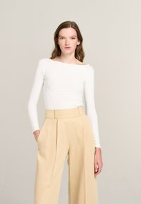 White long-sleeve top with a boat neckline, paired with high-waisted, pleated beige trousers. Minimalist design, smooth texture.
