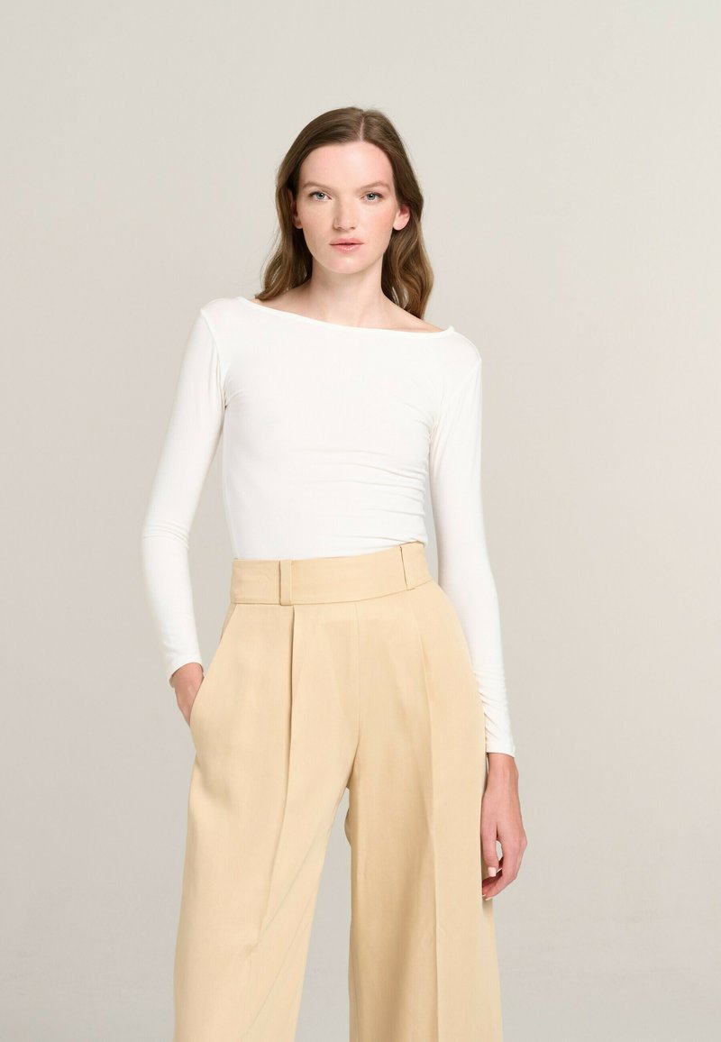 White long-sleeve top with a boat neckline, paired with high-waisted, pleated beige trousers. Minimalist design, smooth texture.