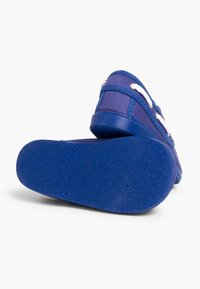 Zapato de lona azul con suela de goma texturizada, cordones blancos y ojales de metal. Presenta puntera redondeada y detalles de costura.