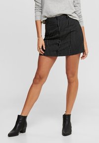 Minifalda a rayas en blanco y negro con cierre de botones en la parte frontal. Combinada con botas de tobillo negras y una sudadera gris. Textura de tela suave.