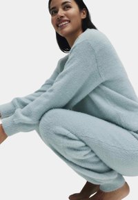 Světlomodrý chlupatý domácí souprava obsahující svetr volného střihu s pokleslými rameny a odpovídající zúžené kalhoty s elastickými manžetami.