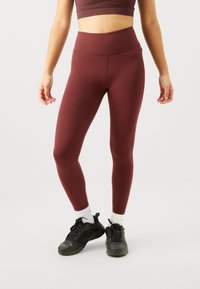 Bordeaux leggings laget av elastisk stoff med høy midje, jevn tekstur og tettsittende design. Båret med svarte treningssko.