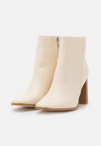 Botas de tobillo de imitación cuero beige con punta afilada, cierre con cremallera en la parte trasera y tacón cuadrado texturizado.