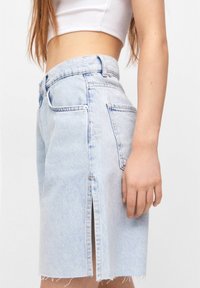 Falda de mezclilla azul claro con dobladillo deshilachado, detalle de abertura frontal y bolsillos estándar. El material es suave y tiene una textura lisa.