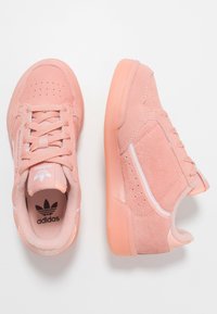 Sneaker in scamosciato rosa chiaro con superficie testurizzata, design con lacci e dettagli bianchi. Presenta una suola in gomma e fori decorativi sulla punta.