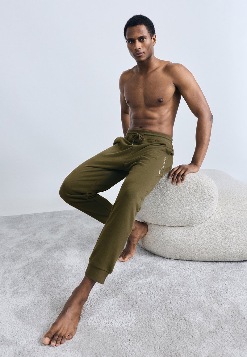 Πράσινο ελιάς παντελόνι φόρμας από απαλό ύφασμα, με ρυθμιζόμενη μέση με κορδόνι και ριμπ μανσέτες, σε μινιμαλιστικό σχέδιο.