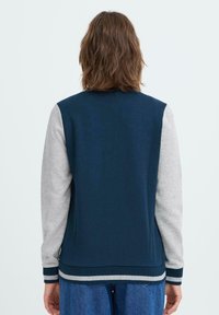 Tumesinine ja hall sweatshirt, millel on soonikkoelus ja -kätised. Omab siledat tekstuuri lihtsa disaini ja kontrastsetes värvitoonides varrukatega.
