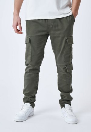 Pantalones cargo verde oliva con múltiples bolsillos laterales, piernas ajustadas y una tela suave y texturizada. Combinados con zapatillas blancas.