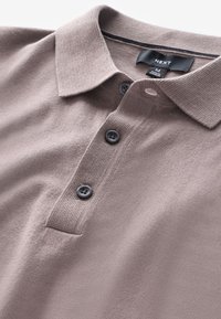 Bruine polo met een gestructureerde stof, voorzien van een drieknopenknoopsluiting, met zwarte knopen en een kraag. Label toont maat medium.