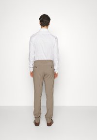 White dress shirt with small blue polka dots, paired with beige trousers. Visible back details include a collar and tailored fit. Brown shoes.