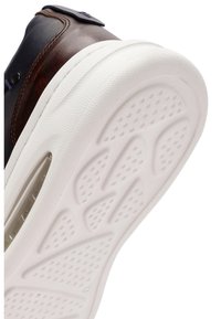 Sneaker con tomaia in pelle marrone e suola in gomma bianca. La suola presenta motivi di grip testurizzati e un dettaglio con finestra trasparente.