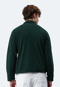 Dunkelgrüne Fleecejacke mit entspannter Passform, langenÄrmeln, einem leicht verkürzten Saum und einer weichen Textur, von hinten betrachtet.