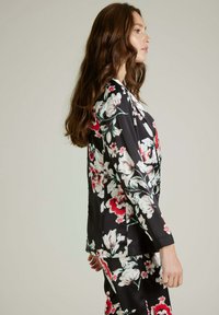 Veste en satin noir à imprimé floral, ornée de fleurs roses et blanches. Présente une coupe décontractée, des manches longues et un col.