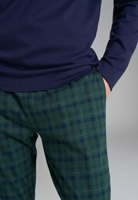 Camicia a maniche lunghe blu navy abbinata a pantaloni a quadri verdi con quadrati blu scuro e sottili righe bianche, che enfatizzano un design e una texture strutturati.