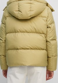 Puchowa, kapturowa kurtka w jasnym oliwkowym kolorze o matowym wykończeniu, z poziomymi przeszyciami i luźnym krojem.