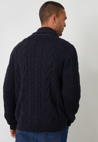 Suéter de punto cableado de color azul marino con cuello y puños acanalados. Presenta patrones texturizados; diseñado para un ajuste relajado con un hilo grueso.
