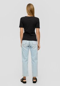 Zwart rib T-shirt met korte mouwen, gecombineerd met lichtblauwe rechte jeans. De jeans hebben een onafgewerkte zoom en minimale details, gedragen met zwarte sandalen.