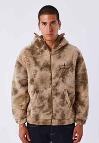 Felpa con zip color sabbia in pile, con una superficie texturizzata e soffice. Presenta un cappuccio, tasche laterali e sottili accenti a motivo scuro.