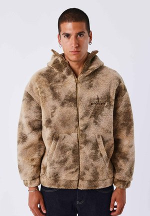 Tan fleece zip-up hoodie met een textuur van een pluche oppervlak. Bevat een capuchon, zijzakken en subtiele donkere patroonaccenten.