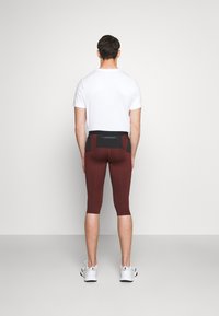 Leggings burdeos con un diseño ajustado, cortados por debajo de la rodilla, combinados con una camiseta blanca; cuentan con una cinturilla negra y bolsillos.