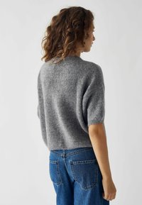 Maglione grigio corto con maniche corte a sbuffo e finitura testurizzata, abbinato a jeans in denim blu con tasche posteriori.