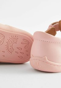 Rosa Babyschuhe aus synthetischem Material, mit einer strukturierten Sohle, die ein Katzendesign aufweist, und hellbraunen Akzenten am Riemen.