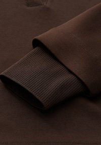 Braunes Langarmshirt mit gerippten Bündchen und glatter Textur, versehen mit einem Halbreißverschluss am Kragen und einfarbig ohne Muster.