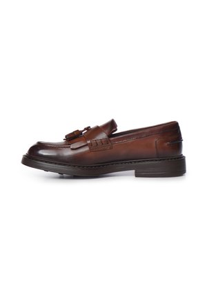 Mocasín de piel marrón con borla, puntera con costura en forma de delantal y suela gruesa y oscura, mostrado de perfil sobre un fondo blanco.