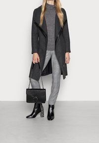 Harmaa villasekoitetakki mustilla nahka-yksityiskohdilla, harmaa neulepaita, ruudulliset housut, musta krokotiilinpainokuvioitu käsilaukku ja mustat nilkkurit kuvioidulla korolla.