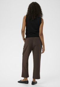 Zwarte mouwloze top gecombineerd met bruine rechttoe-rechtaan broek, voorzien van zijzakken en een effen textuur, aangevuld met zwarte platte schoenen.