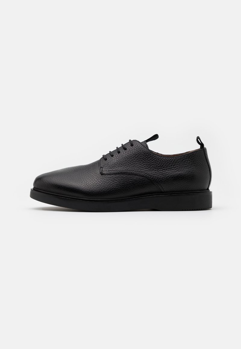 Chaussure noire en cuir à petit talon avec lacets, surface texturée, languettes sur la languette et le talon, vue de côté extérieur sur fond blanc.