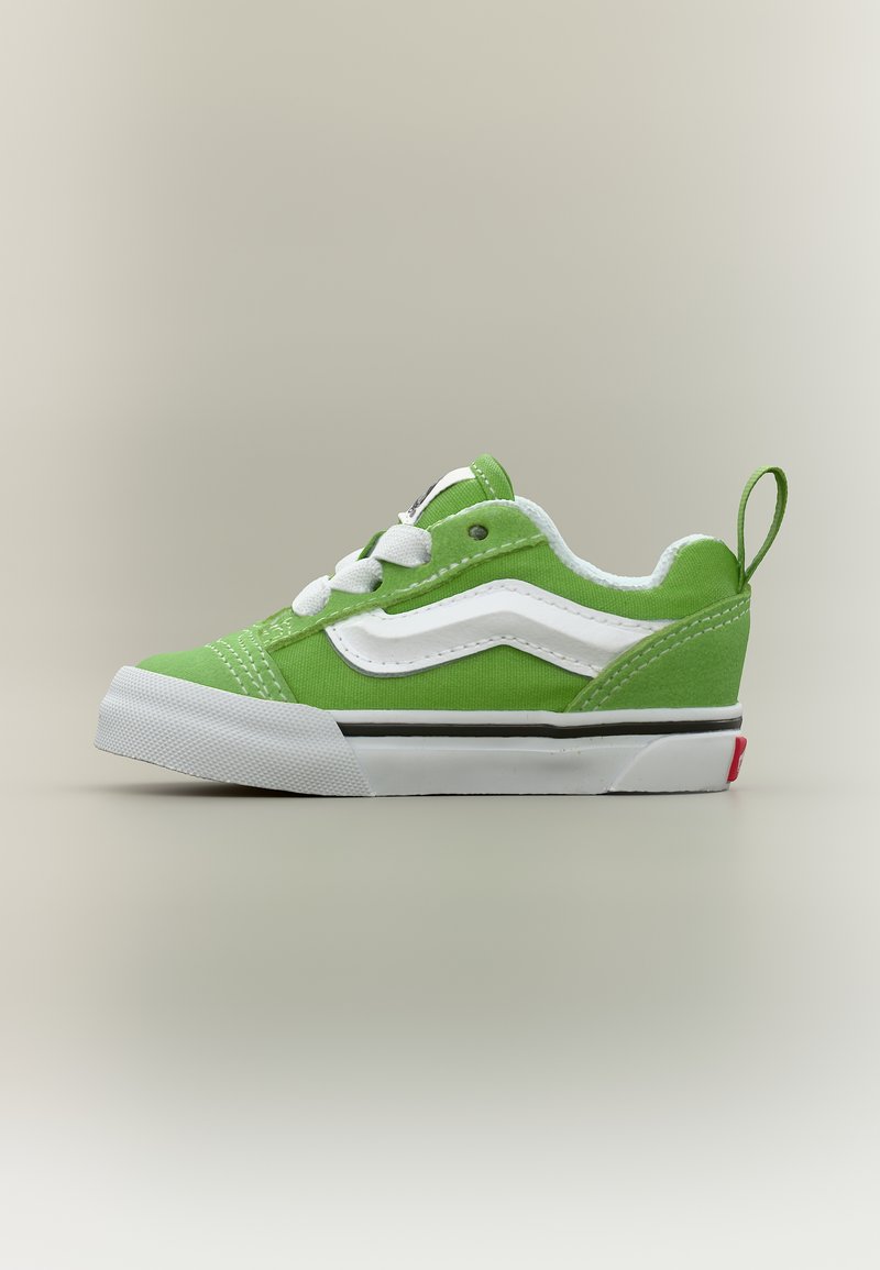 Baskets en toile verte avec lacets blancs, bande latérale ondulée blanche, semelle en caoutchouc blanche et tirette au talon sur un fond neutre.