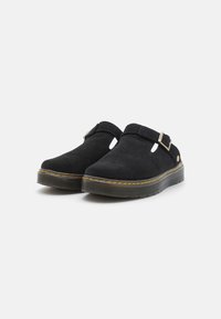 Crne nubuk slip-on klompe s podesivim kopčama, žutim šavovima i debelim teksturiranim gumenim potplatima na jednobojnoj bijeloj pozadini.
