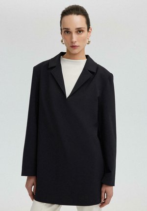 Czarny płaszcz z długimi rękawami i klapami, w oversize'owym fasonie, wykonany z gładkiego materiału. Posiada charakterystyczny dekolt w kształcie litery V. Minimalistyczny design.