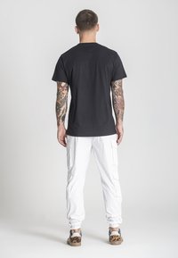 Černé bavlněné tričko s krátkým rukávem, kombinované s bílými cargo kalhotami s bočními kapsami a vzorovanými teniskami. Celkově minimalistický design.