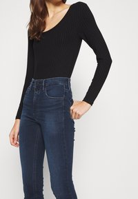 Black ribbed bodysuit with a scoop neckline paired with high-waisted dark blue jeans featuring a smooth texture and two-button closure.