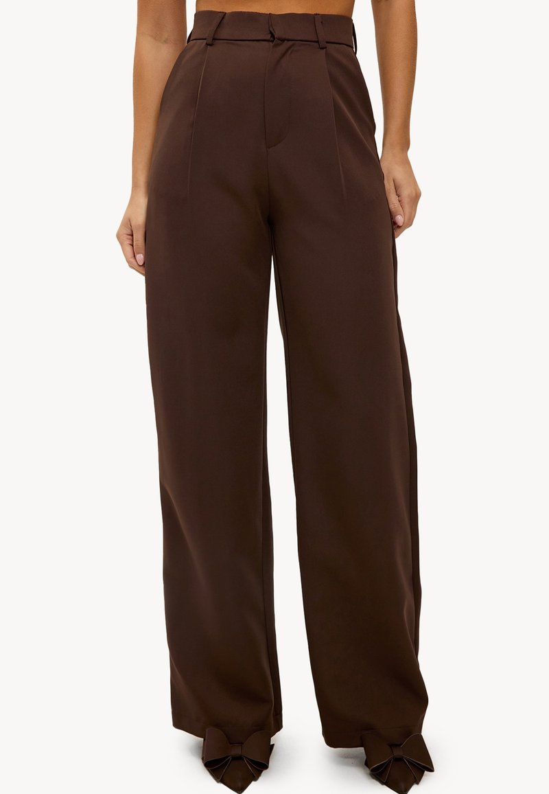 Un pantalon large marron avec une taille haute, un devant plissé et des accents en forme de nœud à l'ourlet. Confectionné dans un tissu lisse pour un look ajusté.