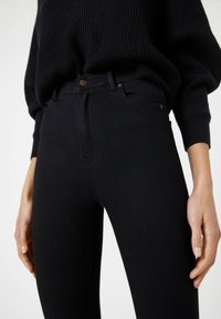 Jeans ajustados de tiro alto en negro, confeccionados en denim con una textura suave, que presentan un cierre frontal con botón y bolsillos laterales.