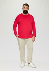 Rotes Langarm-T-Shirt aus Baumwolle, kombiniert mit cremefarbenen Hosen und weißen Sneakers. Einfaches Design ohne sichtbare Muster.