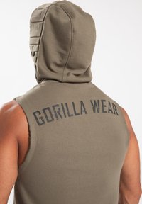 Mouwloze, olijfgroene hoodie met een gestructureerde capuchon, met "GORILLA WEAR" gedrukt op de achterkant in het zwart. Zachte, katoenen stof.