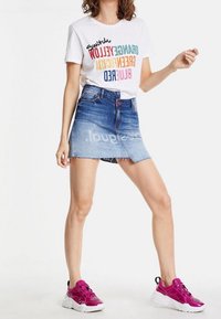 Camiseta blanca con texto colorido, falda mini de mezclilla con degradado desvaído y zapatillas rosas con suelas blancas y detalles negros.