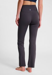 Mörkgrå yogabyxor med hög midja, med en liten blå chevrondetalj bak och en figurnära design som vida ut något vid anklarna.