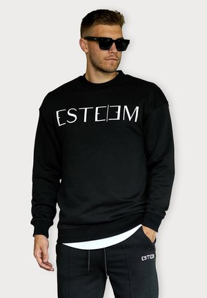 Schwarzer Sweatshirt mit weißem "ESTEEM"-Text auf der Brust, Rundhalsausschnitt und gerippten Bündchen, kombiniert mit schwarzen Hosen und reflektierenden Sonnenbrillen.