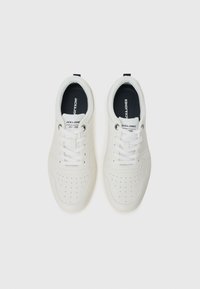 Zapatillas blancas con detalles perforados y forro interior negro, que presentan cordones y una marca en la lengüeta, sobre un fondo liso.