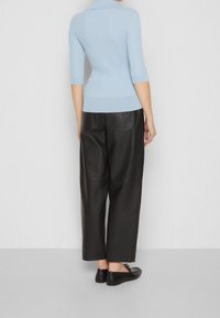 Jasnoniebieski sweter z prążkowanego dzianiny z kołnierzykiem, zestawiony z czarnymi, szerokimi spodniami z wysokim stanem wykonanymi ze skóry oraz czarnymi, płaskimi butami.