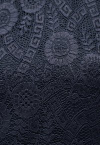 Μαύρο δαντελένιο ύφασμα με λουλουδάτα και γεωμετρικά μοτίβα που περιλαμβάνει περίπλοκο δίχτυ και συμπαγείς κεντητές περιοχές.