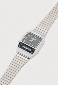 Ψηφιακό ρολόι σε ασημί τόνο με ορθογώνιο καντράν, μαύρο καντράν, λευκούς αριθμούς και μπρασελέ από ανοξείδωτο ατσάλι. Διαθέτει λογότυπο της μάρκας και διπλές οθόνες.